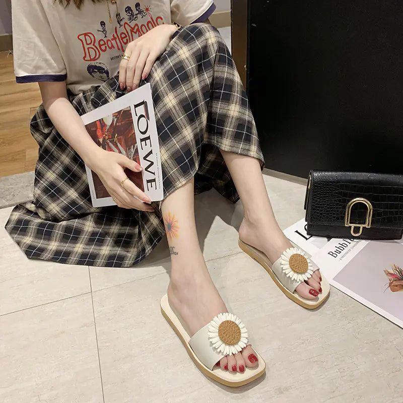 Close up of black and beige slide sandals with large daisy flower accents on the strap
