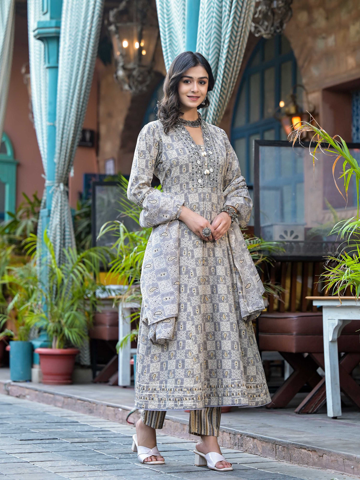 A woman wearing a grey embroidered and printed flared kurta set with matching pants and dupatta.