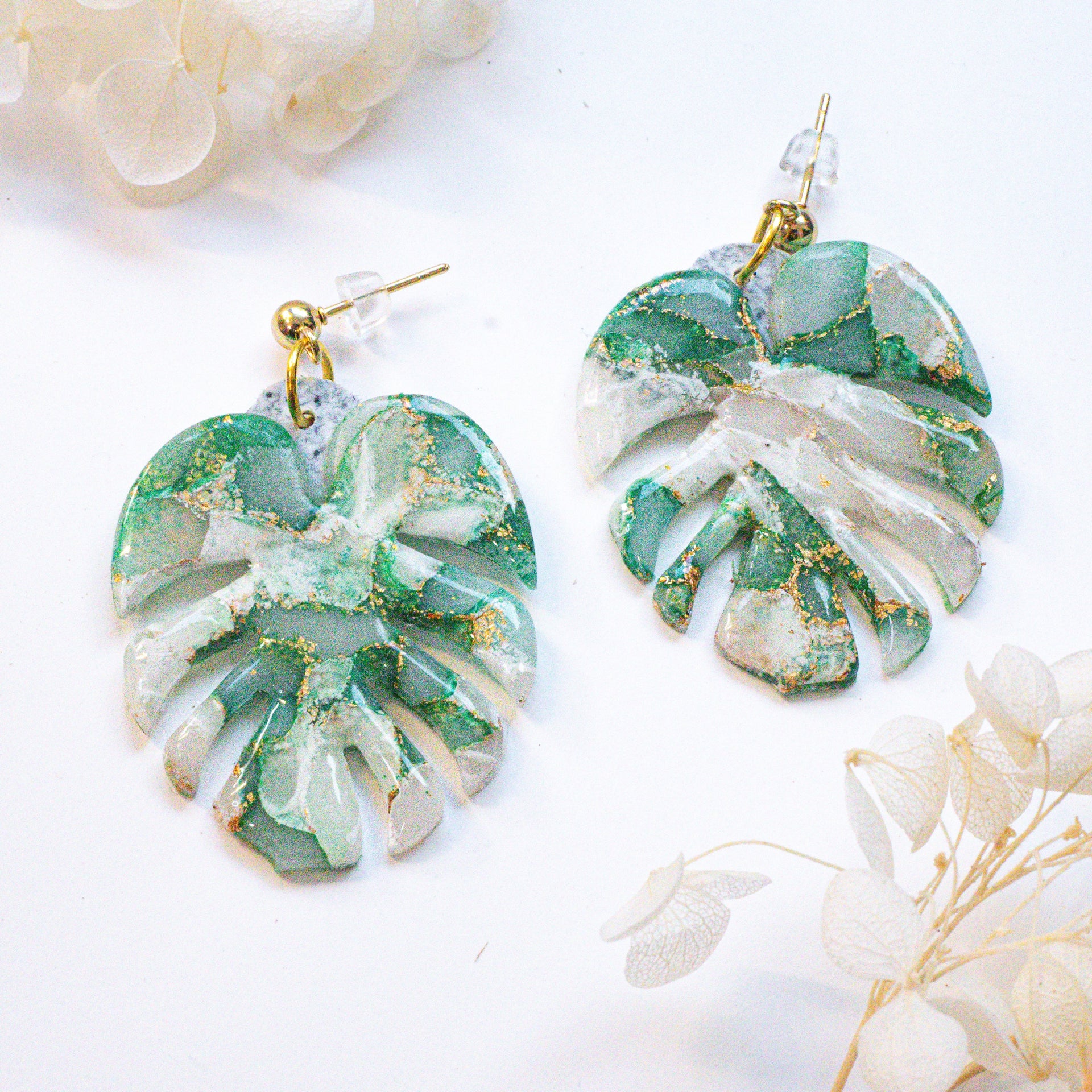 Monstera leaf-shaped earrings with green, white, and gold marble pattern and gold foil accents