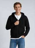 A man wearing a black midweight zip-up hoodie layered over a white t-shirt.