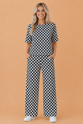 A woman wearing a matching black and white checkerboard print lounge set with a crew neck tee and wide-leg pants.