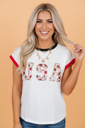 Woman wearing a white short-sleeve t-shirt with USA written in sequin patches, featuring red sleeve trim and black neckline trim.