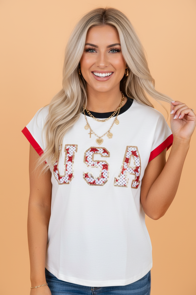 Woman wearing a white short-sleeve t-shirt with USA written in sequin patches, featuring red sleeve trim and black neckline trim.