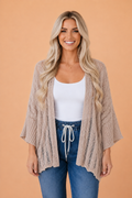 A woman wearing a beige hollowed knit open cardigan with three-quarter sleeves and drop shoulders.