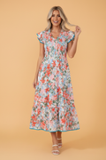 Floral print maxi dress with a smocked bodice and flutter sleeves in a sunny outdoor setting.