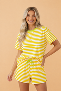 Woman wearing a bright yellow and white striped knit tee and drawstring shorts set with neon green trim
