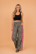 Woman wearing high-waisted leopard print wide-leg pants with hot pink lace side stripes and an adjustable drawstring waist.