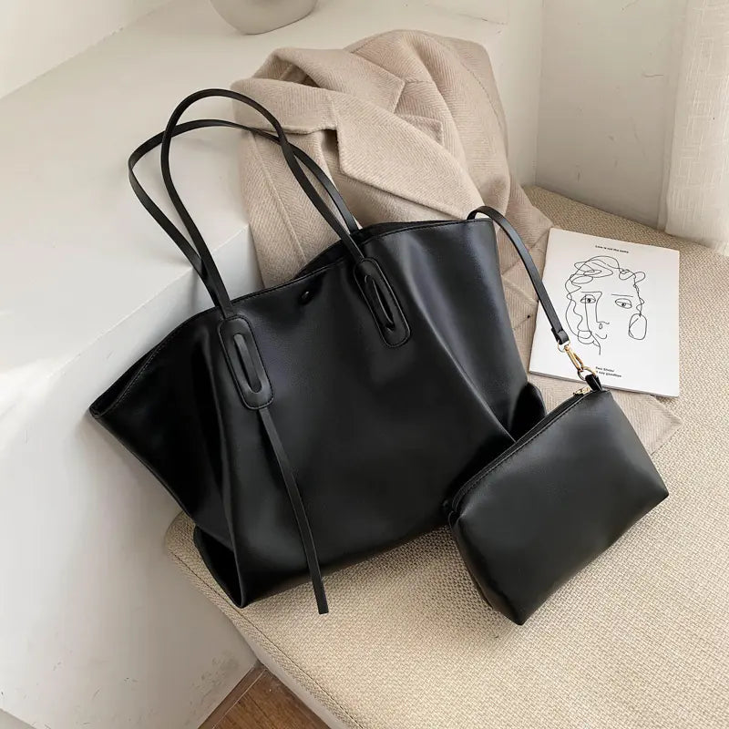 A large solid color shoulder bag in black or white with a matching smaller pouch, shown in a lifestyle setting.