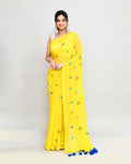 Lemon yellow cotton saree with blue floral embroidery and decorative tassels draped elegantly.