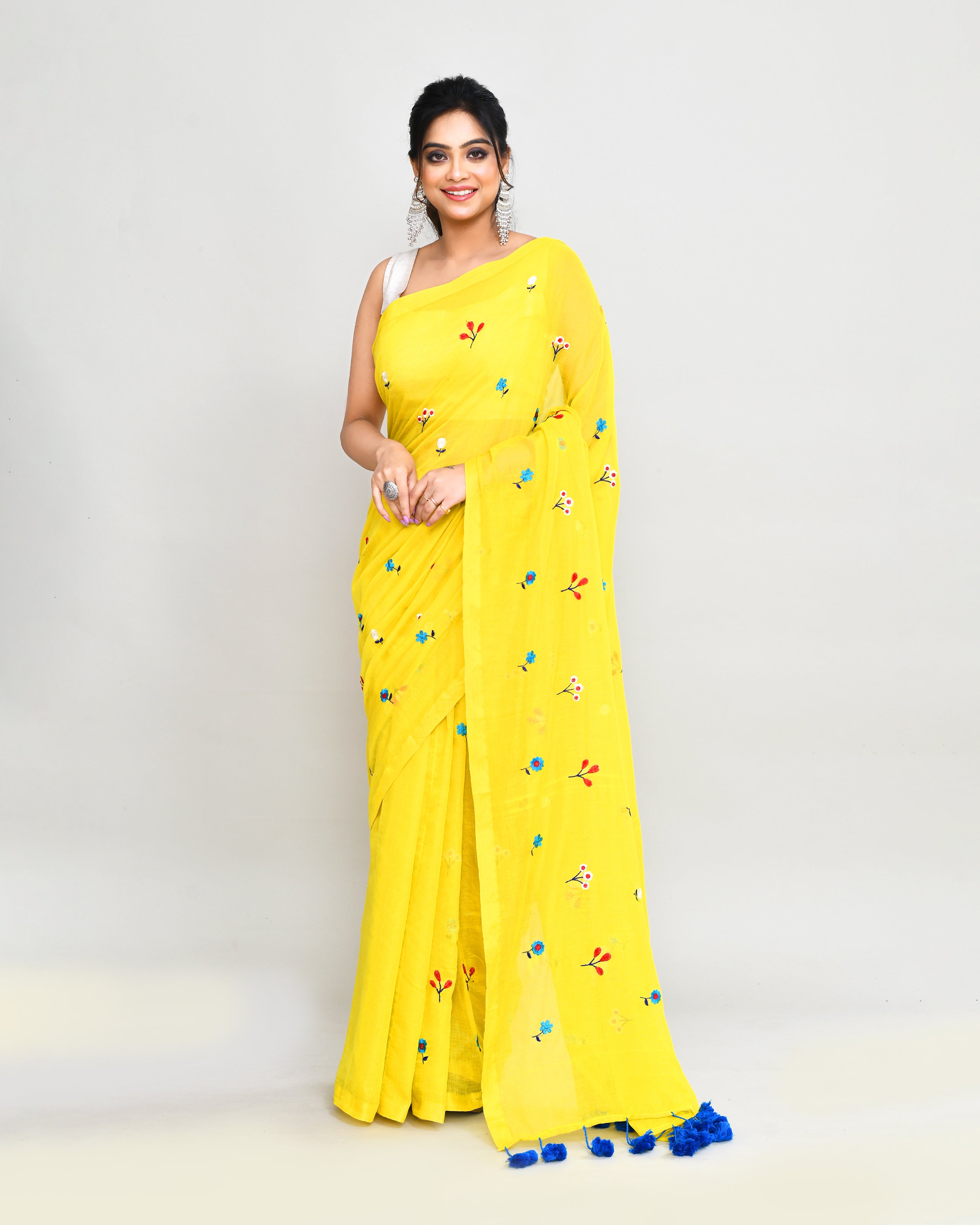 Lemon yellow cotton saree with blue floral embroidery and decorative tassels draped elegantly.