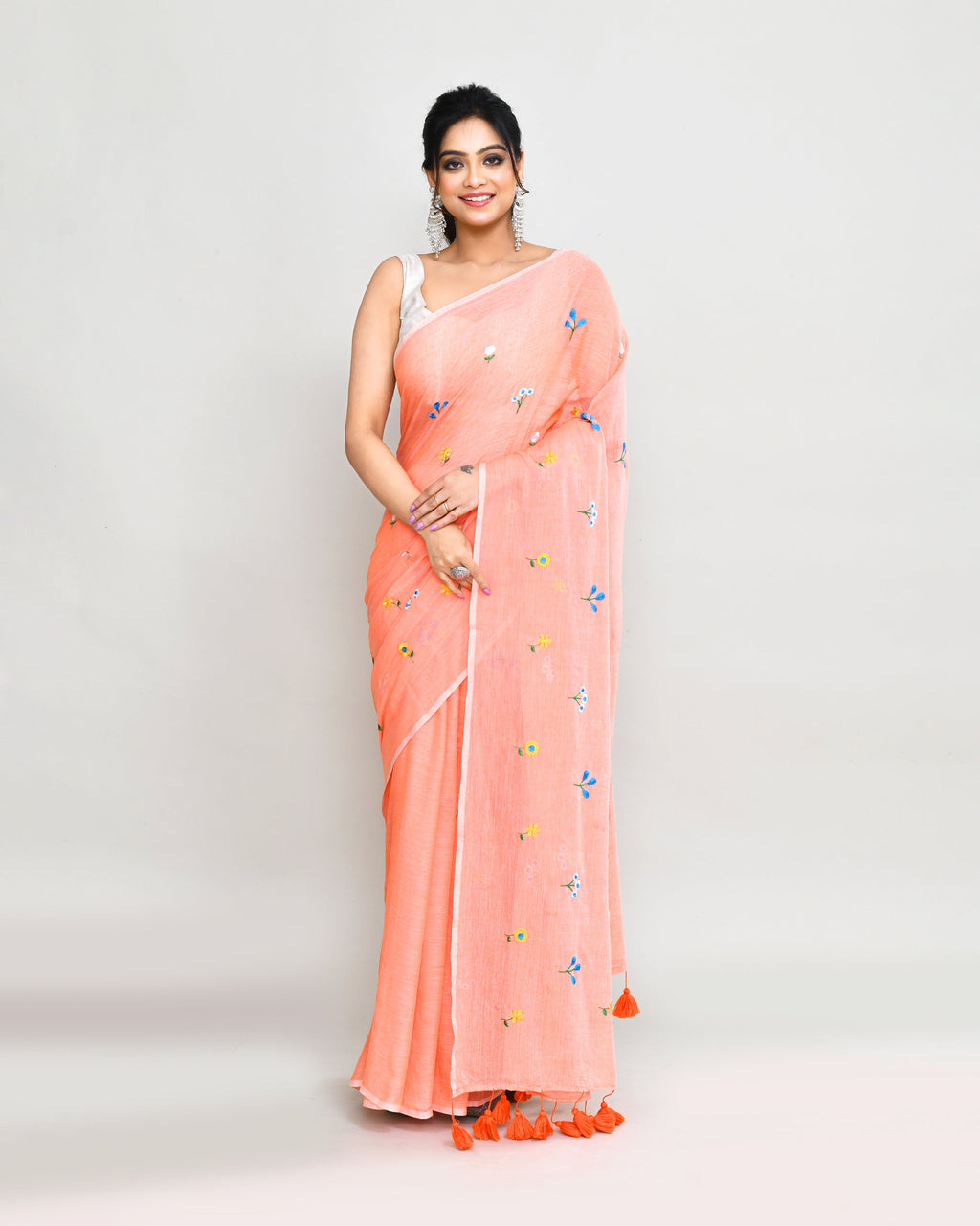 A beautiful salmon-colored cotton saree featuring intricate embroidery and decorative tassels.