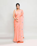 A beautiful salmon-colored cotton saree featuring intricate embroidery and decorative tassels.