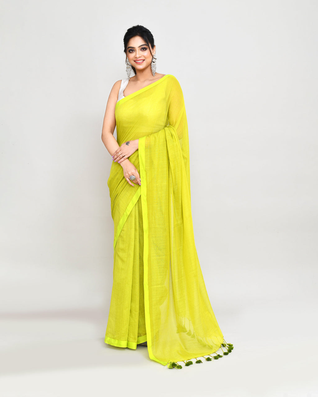 A vibrant lime green Mulmul cotton saree with decorative tassels on the pallu, displayed in a minimalist bohemian style.