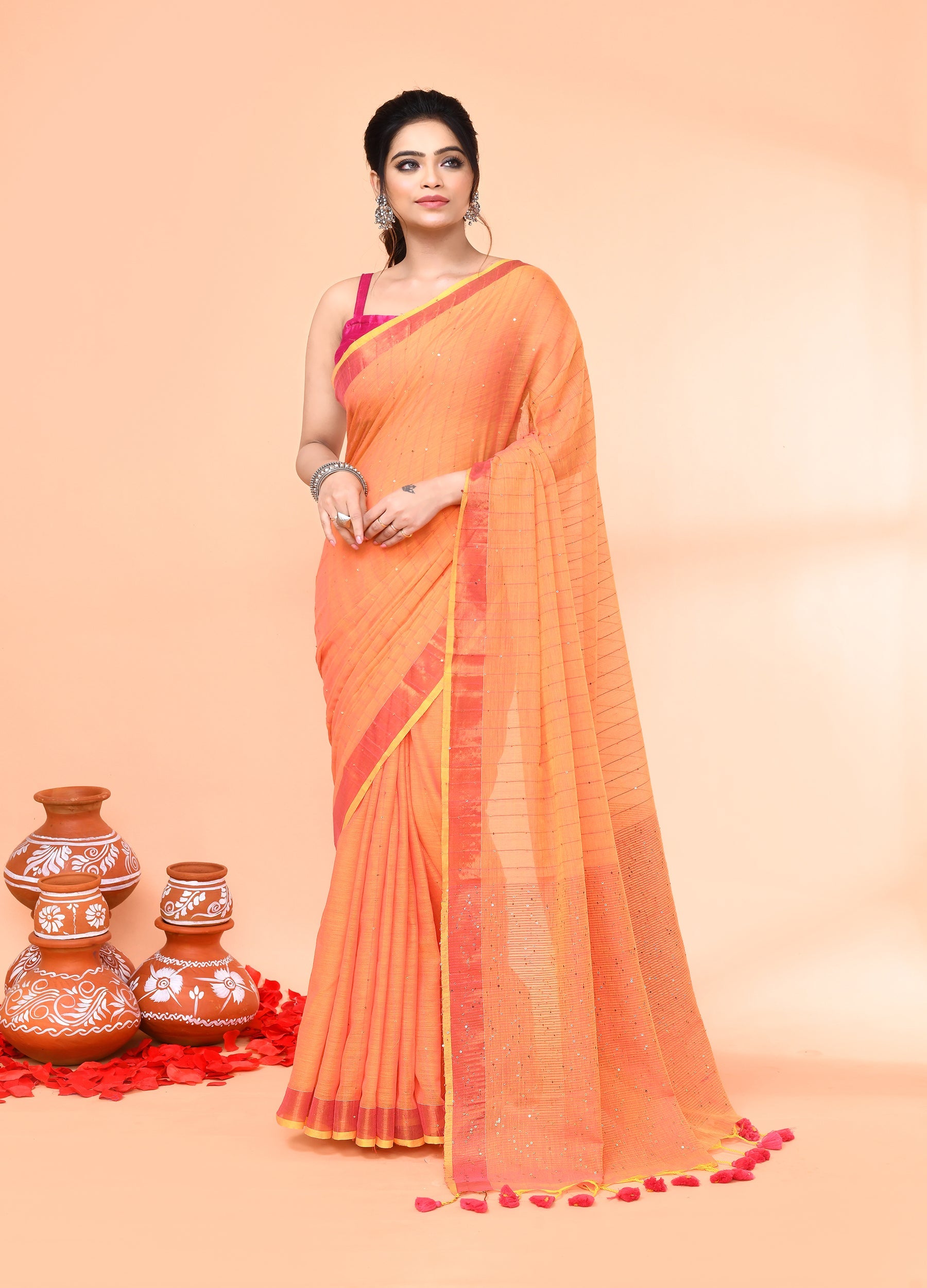 Woman wearing a pale orange cotton handloom saree with delicate sequin detailing and matching blouse