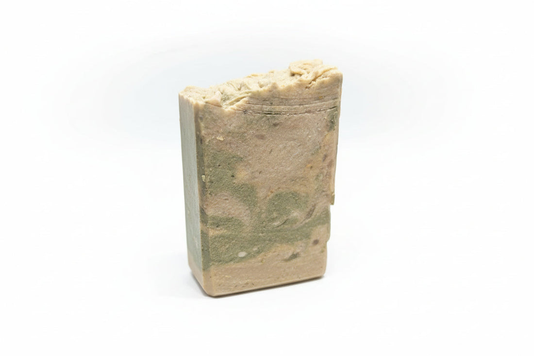 A beige and green marbled soap bar with a wildflower-themed label resting in a woven basket next to a botanical field guide.