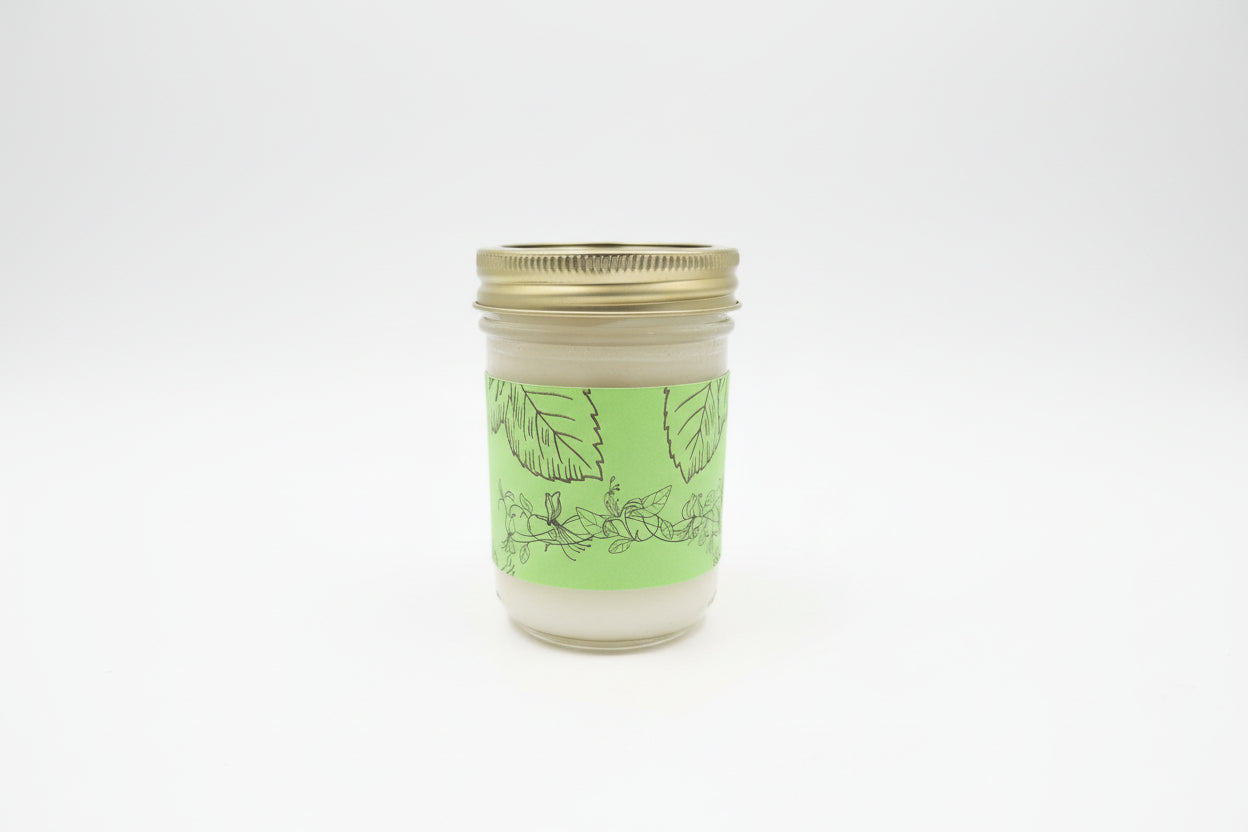 A glass jar of Wildflower Bouquet Whipped Tallow Body Butter sitting on a wooden post in a blooming field of wildflowers.