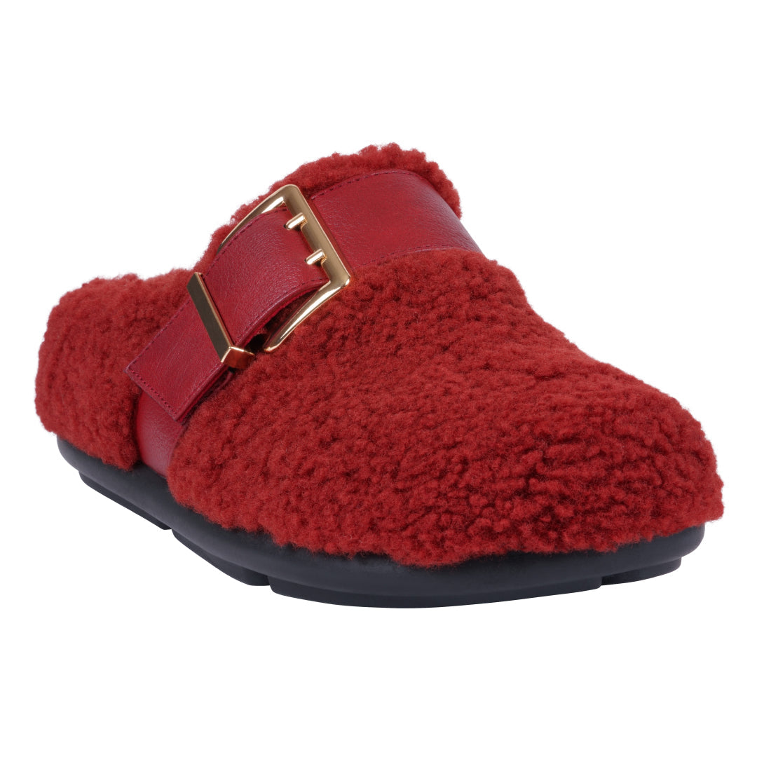 A pair of burgundy faux-shearling mule slippers for women featuring a gold-tone decorative buckle on a strap across the vamp and a black rubberized sole.