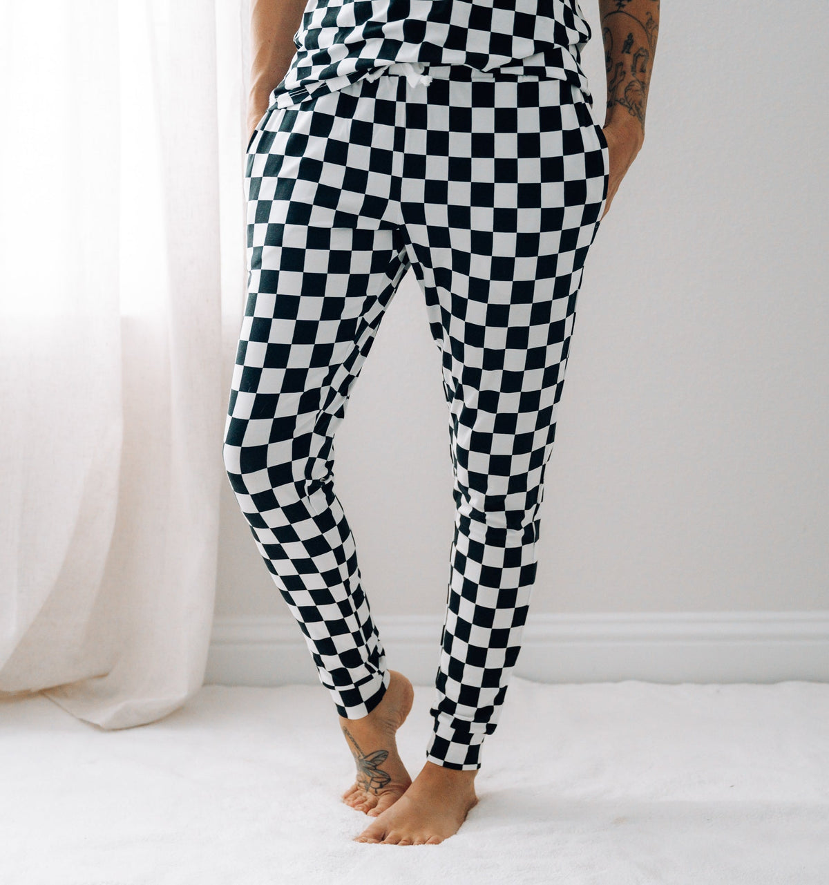 A woman wearing black and white checkered bamboo joggers standing in a bright room.