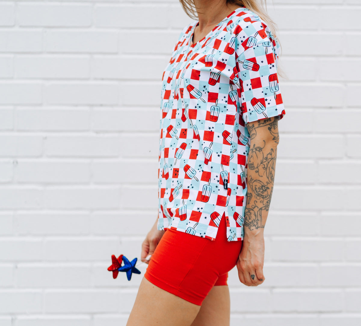 Woman wearing a white v-neck t-shirt with a red and blue bomb pop pattern and solid red biker shorts.