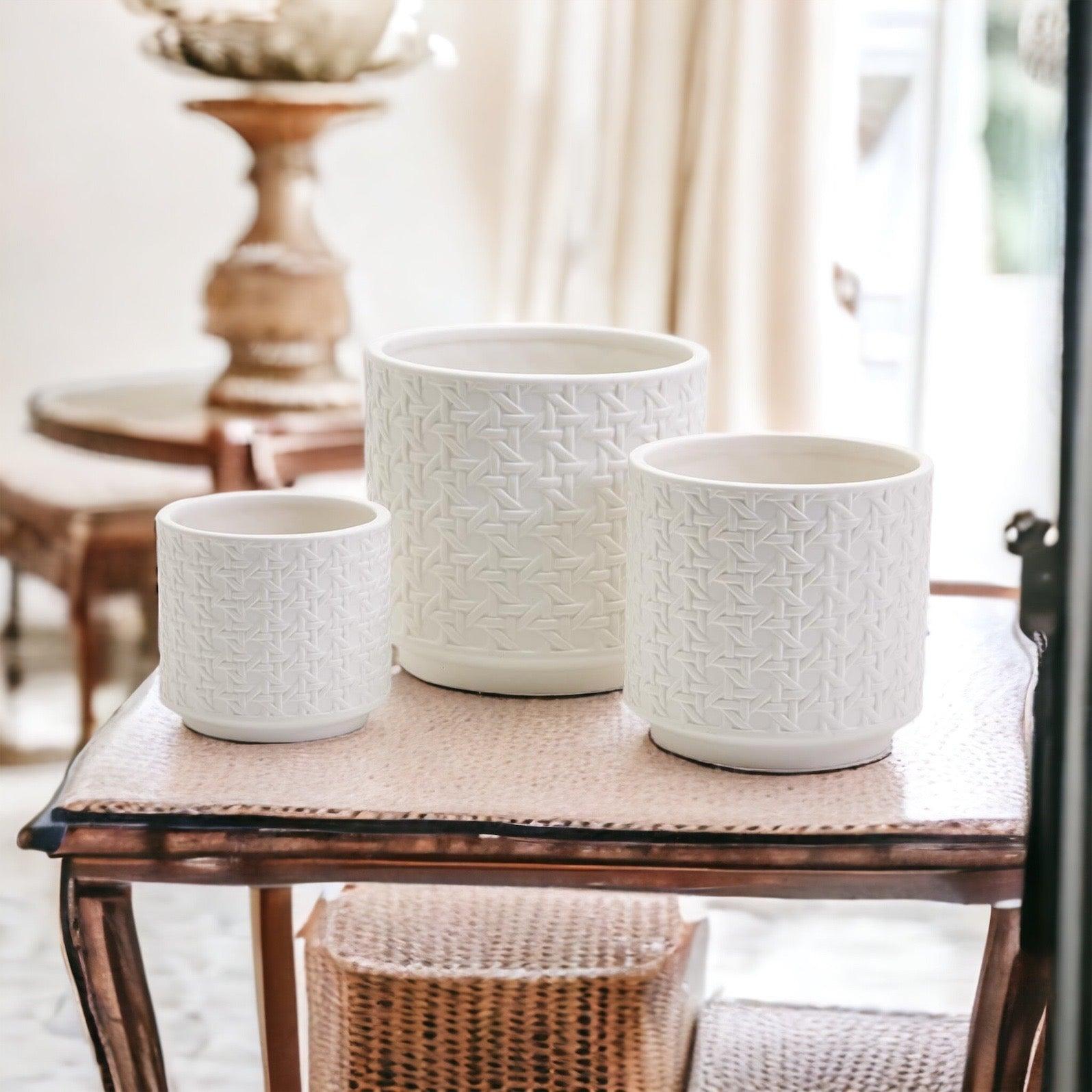 Set of three white ceramic planters with a textured woven webbing pattern sitting on a table.