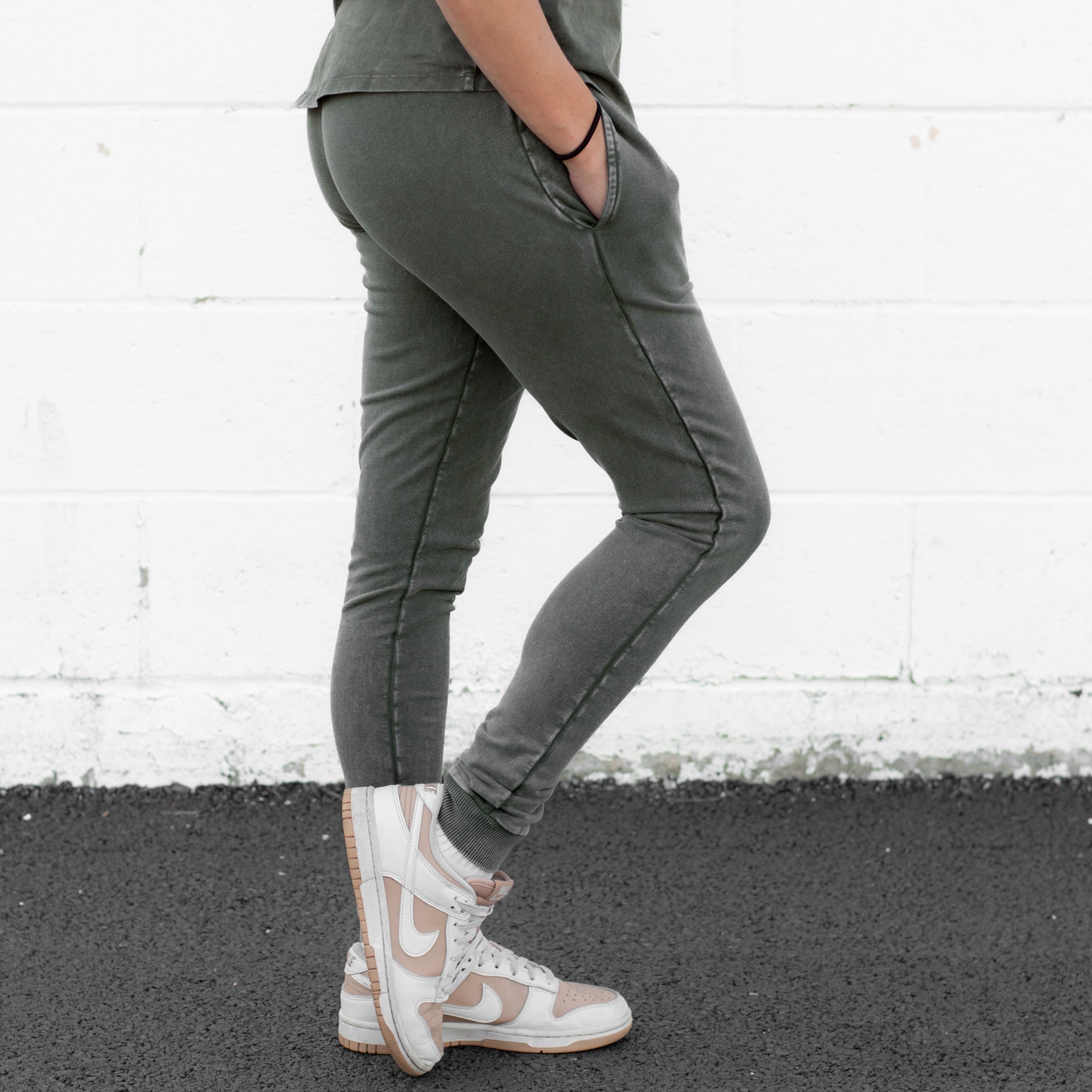 A woman wearing green moss snow wash organic cotton joggers with a matching t-shirt and casual sneakers.