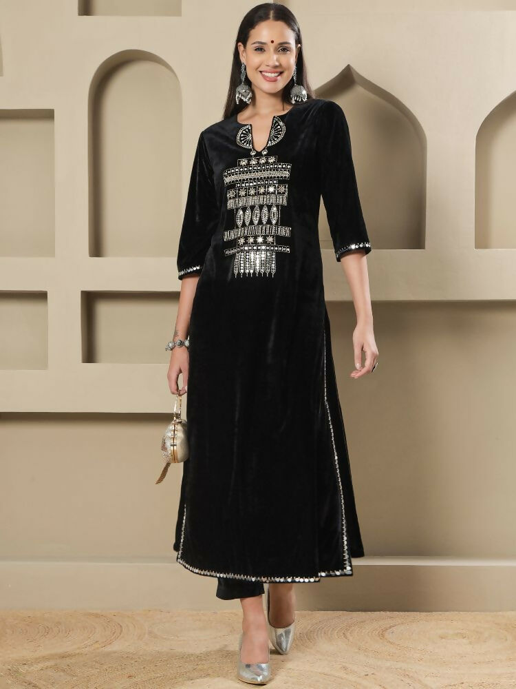 A woman wearing a black velvet kurta set with intricate hand embellishments and three-quarter sleeves.
