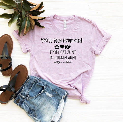 Lavender crew neck t-shirt with You've Been Promoted from Cat Aunt to Human Aunt text design, displayed with sandals and denim shorts.