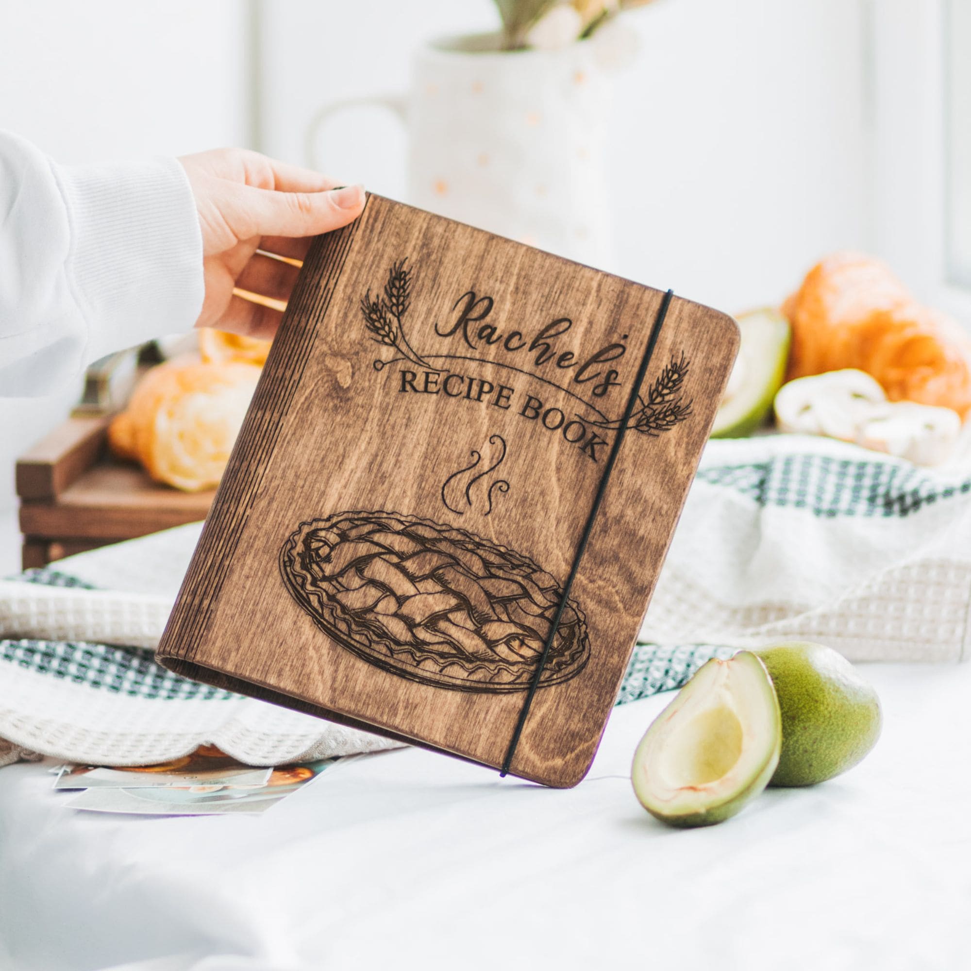 Brown wooden recipe book for pies and tarts with personalized engraving on a kitchen counter.