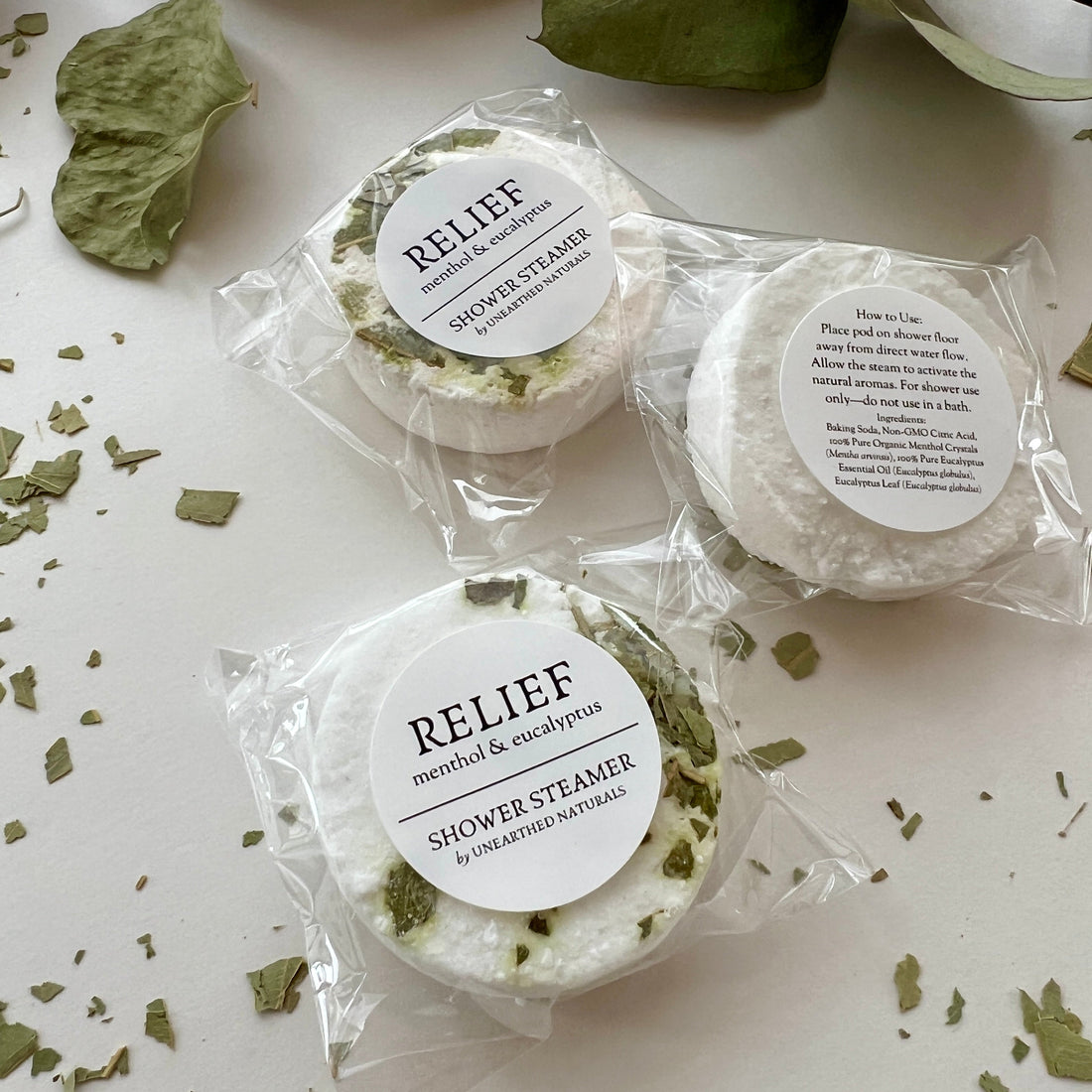 Top view of three round Relief Shower Steamers with dried eucalyptus leaves on a white background