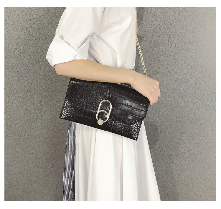 A black crocodile pattern envelope clutch bag with gold-tone chain and circular metal ring clasp being held.