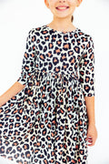 Young girl wearing a beige dress with a black and peach leopard print pattern featuring 3/4 length sleeves and a full skirt.