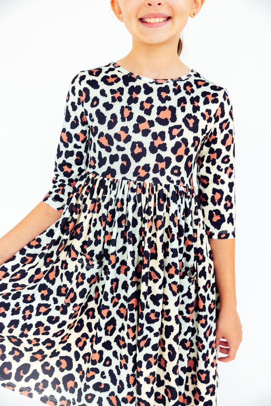 Young girl wearing a beige dress with a black and peach leopard print pattern featuring 3/4 length sleeves and a full skirt.
