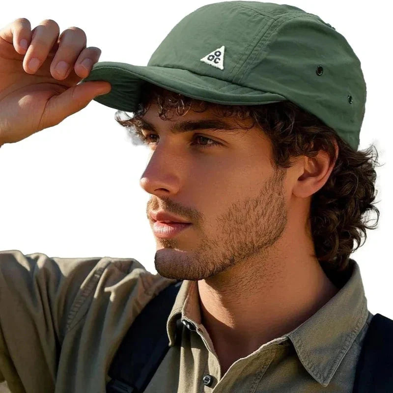 A person wearing a green breathable 5-panel trucker cap with a short brim during an outdoor activity.