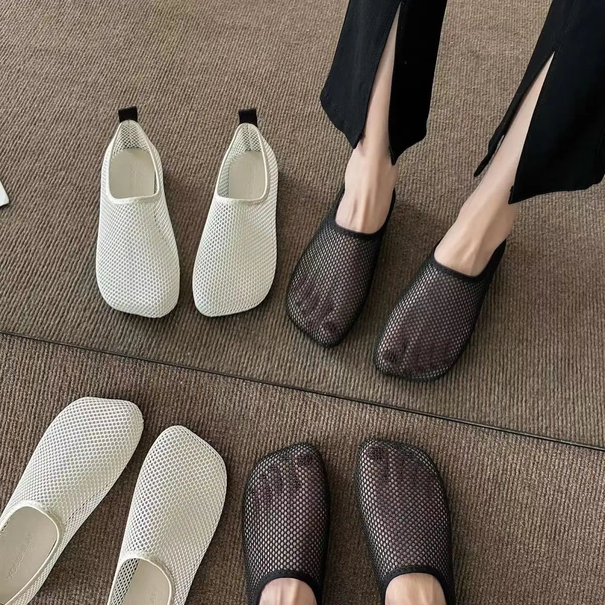 Close up overhead view of feet wearing white and black mesh slip-on sandals on a textured surface.