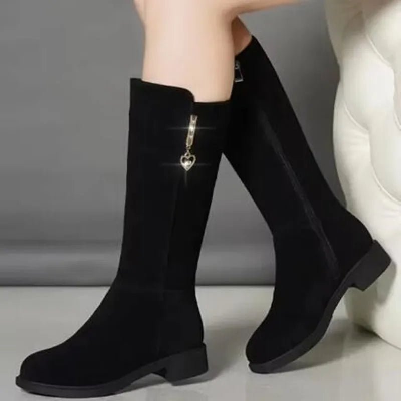 A pair of women's black mid-calf winter boots featuring a small heart charm on the side zipper.