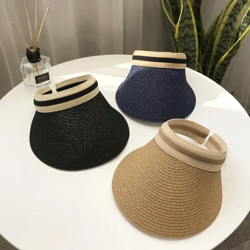 Set of three straw visor hats in black, navy, and natural straw colors, displayed on a table.