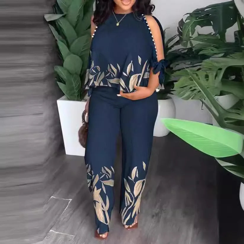 A woman wearing a navy blue two-piece set with a cold-shoulder top and straight-leg pants featuring a leaf print and bead accents.