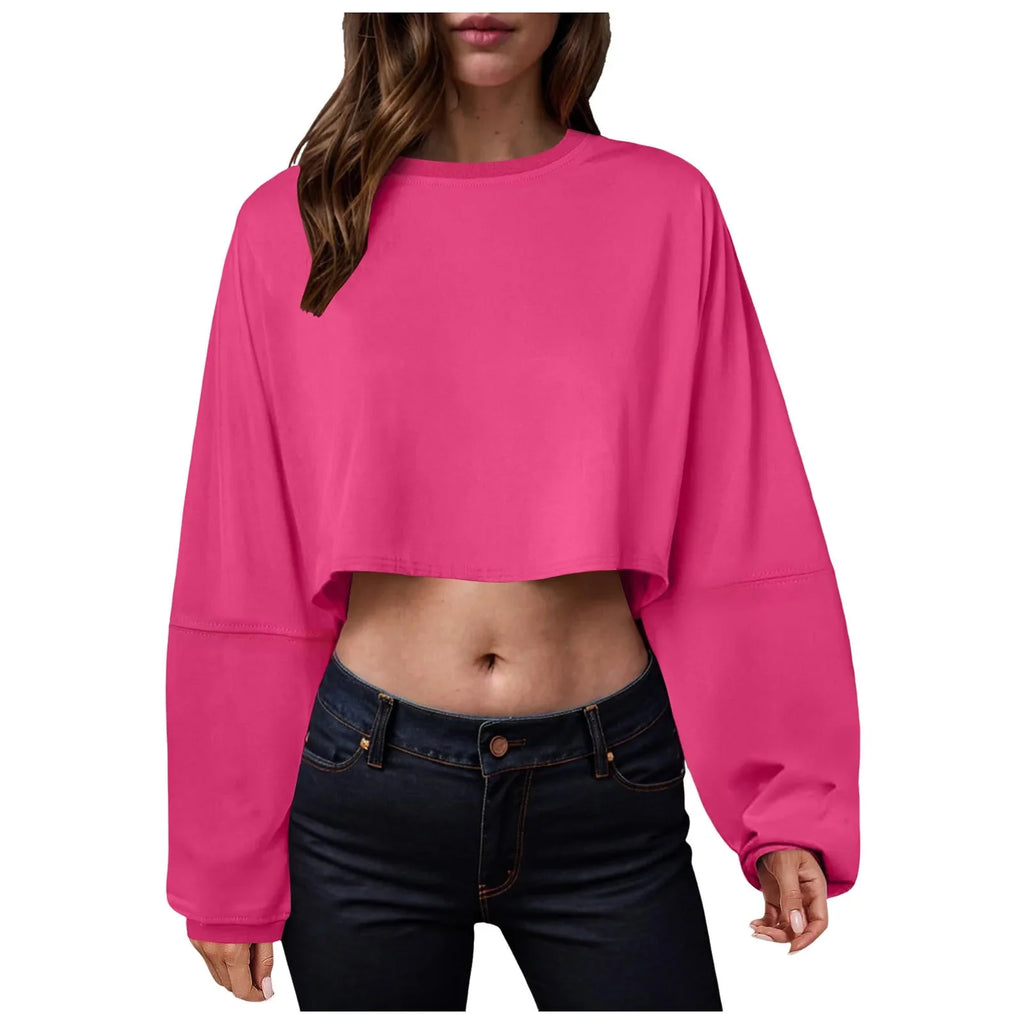 A woman wearing a vibrant pink long-sleeve loose-fit crop top.