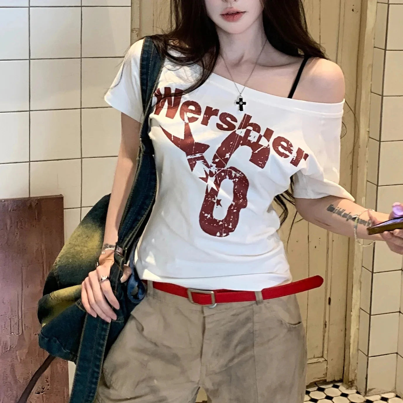 A woman wearing a slim fit white summer t-shirt with letter and star graphics and a skew collar neckline, paired with khaki pants.