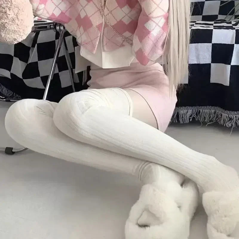 Close-up of a woman wearing white ribbed knee-high socks and fluffy slippers, showcasing the sock texture and length.