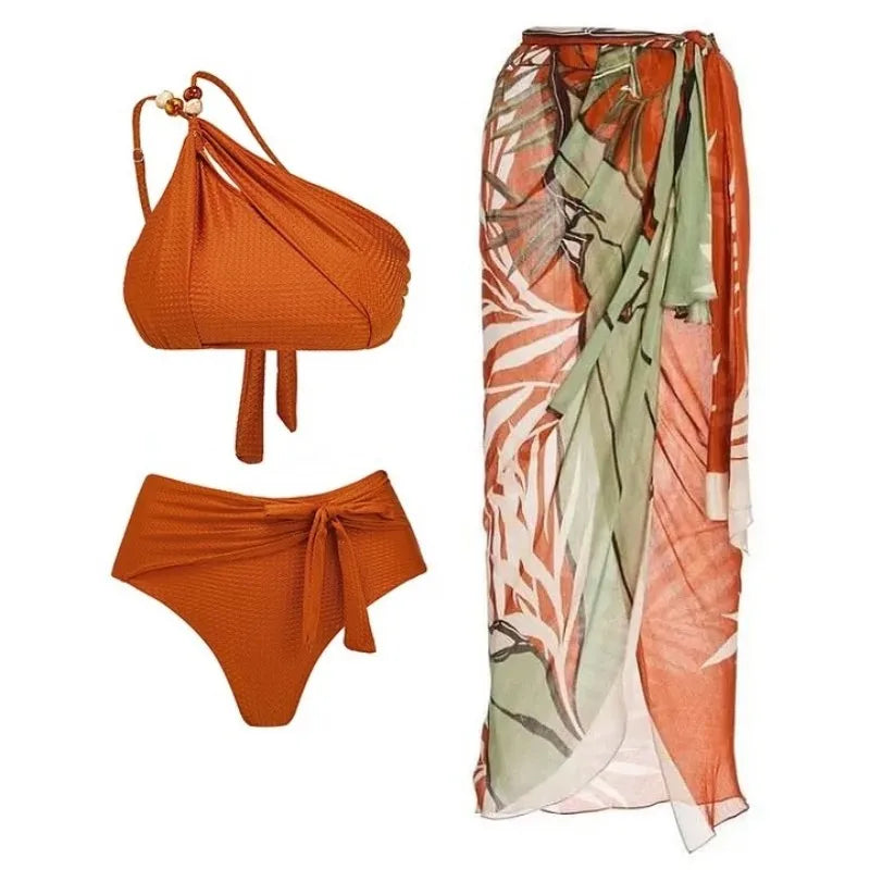 A textured one-shoulder bikini top with high-waisted bottoms and a matching printed sarong wrap.