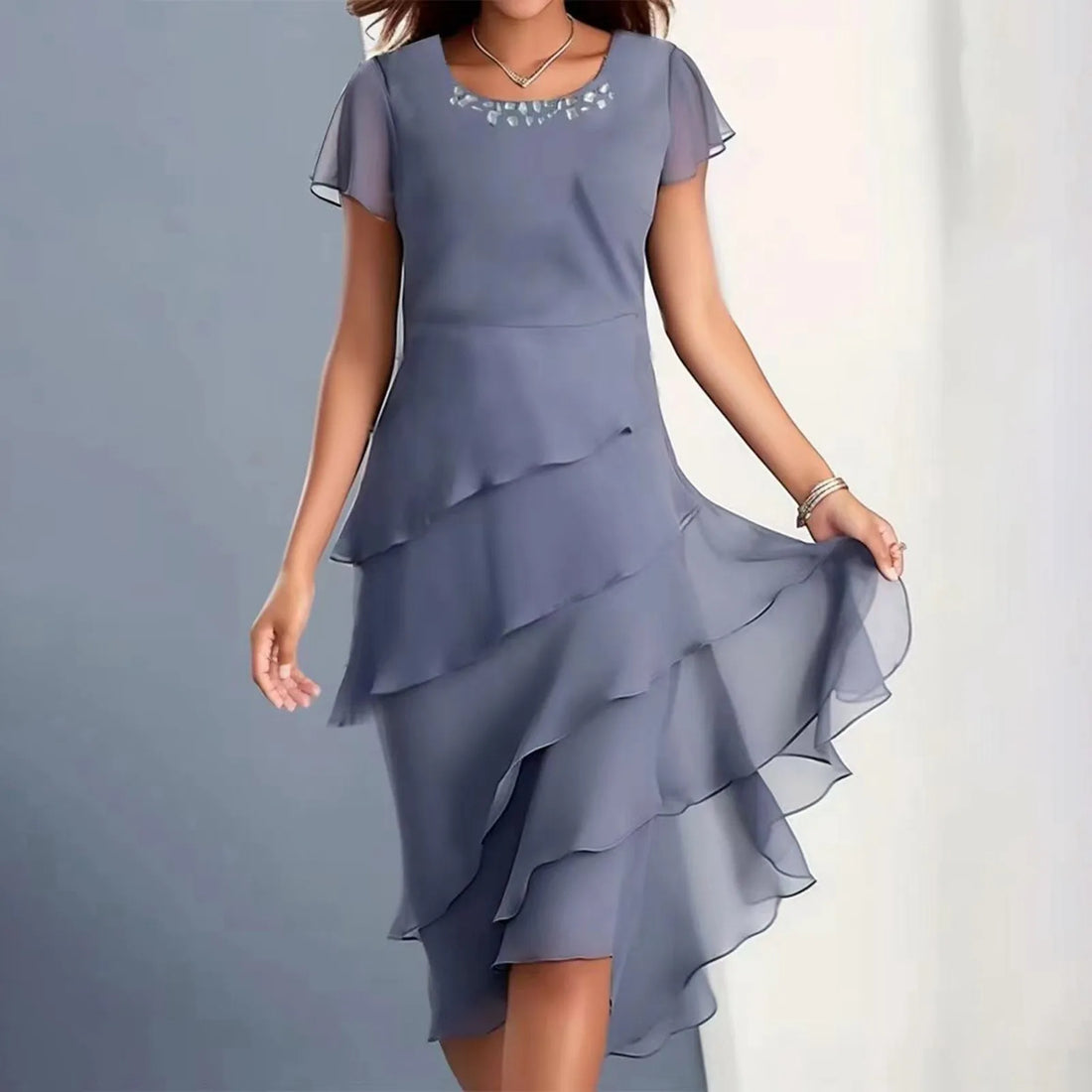 A woman wearing a dusty blue layered chiffon midi dress with a round embellished neckline.
