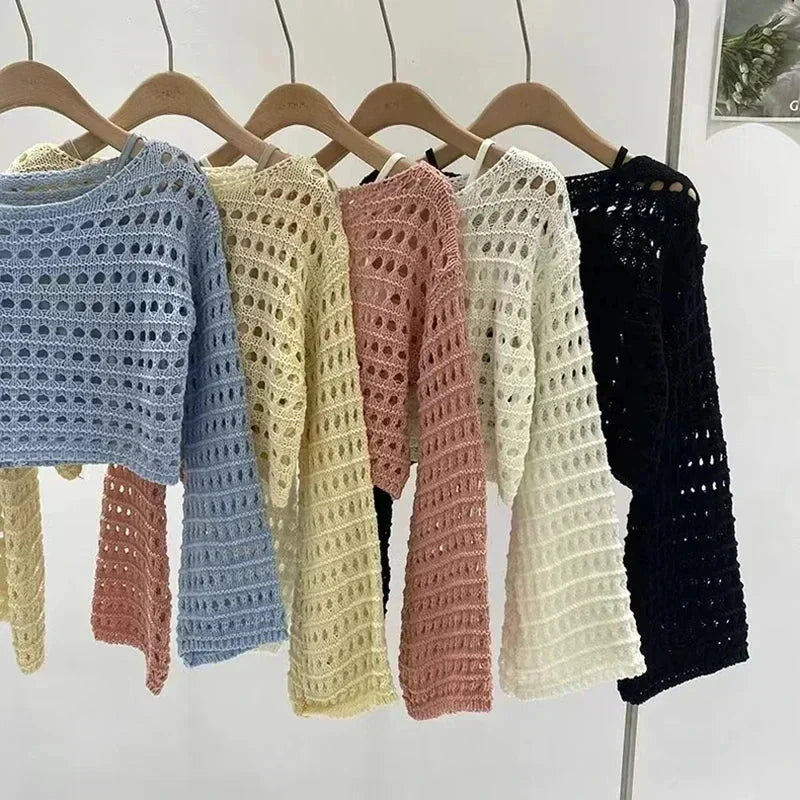 Collection of women's long-sleeve crochet knit tops in various pastel and neutral colors hanging on a rack.