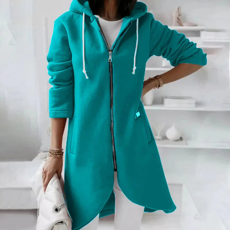 Person wearing a teal hoodie with a zipper in a minimalistic room.