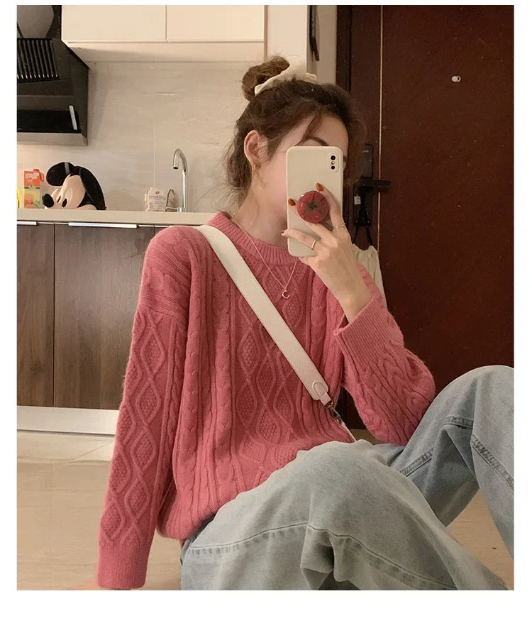 A woman wearing a cozy pink cable knit sweater with long sleeves and a crew neck, paired with light blue jeans.