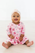 Baby wearing a pink long sleeve bodysuit with smiley face and heart pattern and a twirl skirt bottom.