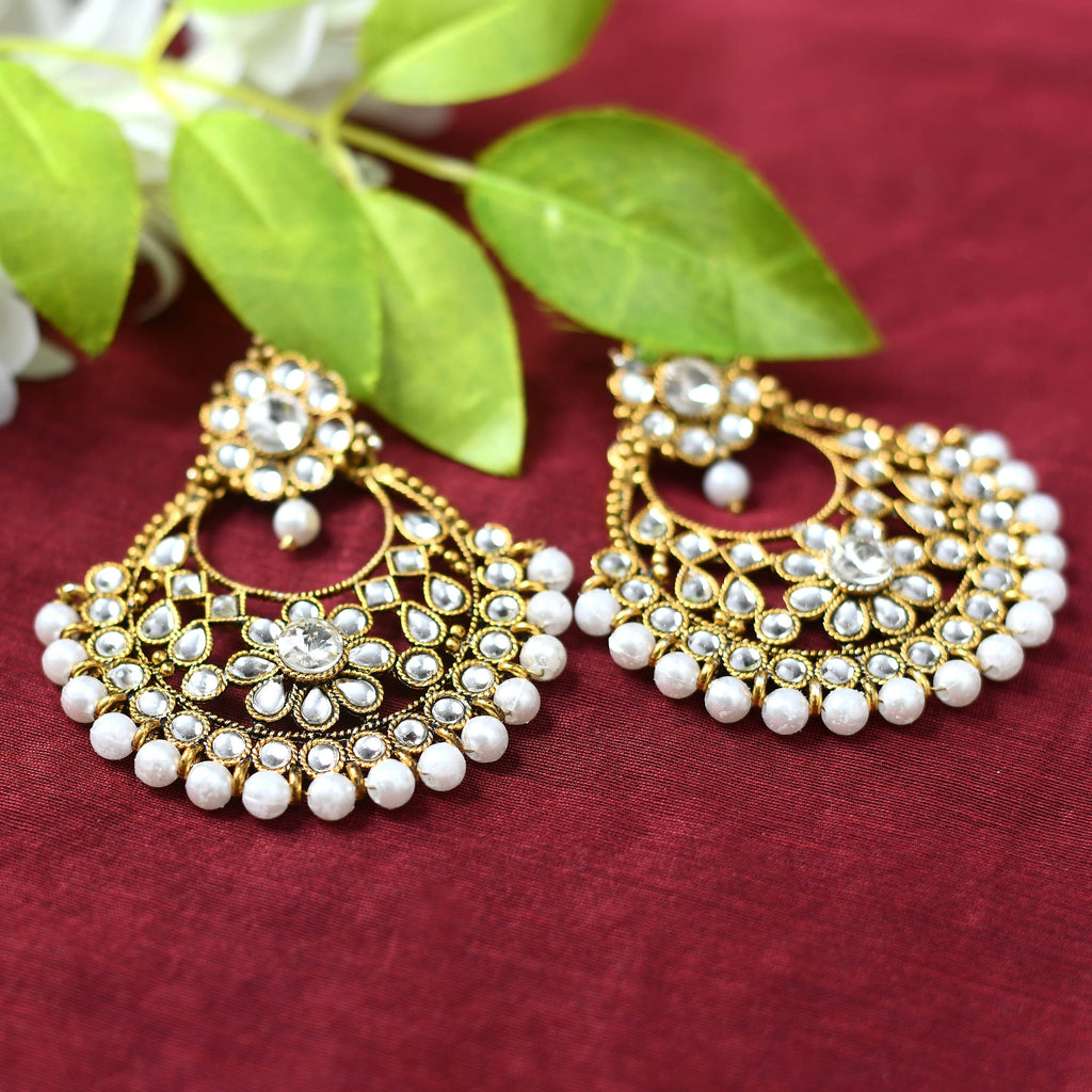 Close-up of elegant golden and white beaded drop earrings on a neutral background.