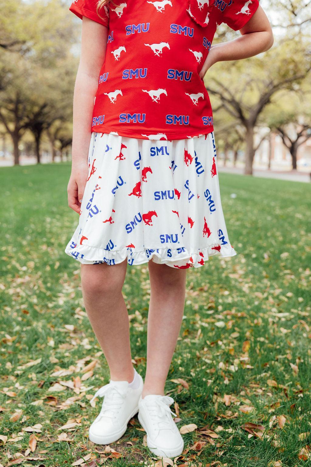 Girl wearing a white skort with SMU Mustangs and logo print, featuring a ruffle hem, paired with a red graphic t-shirt.