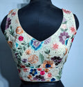 Off-white readymade blouse with multicolor floral embroidery and curved V-neck design.