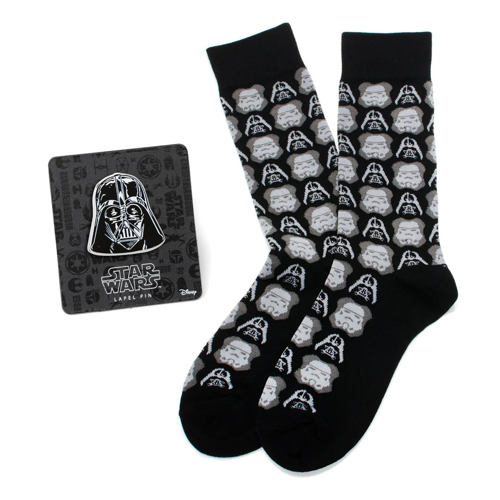 A pair of black crew socks with a repeating pattern of Darth Vader and Stormtrooper helmets next to a Star Wars Darth Vader lapel pin.